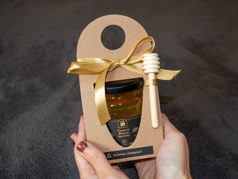 Kézben tartott kis üveges méz arany szalaggal – kézműves céges ajándék dolgozóknak vagy partnereknek.